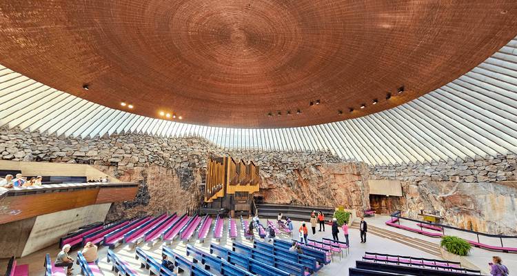 Intérieur d'une église circulaire taillée dans la roche avec plafond en dôme de cuivre et rangées de bancs de couleur.