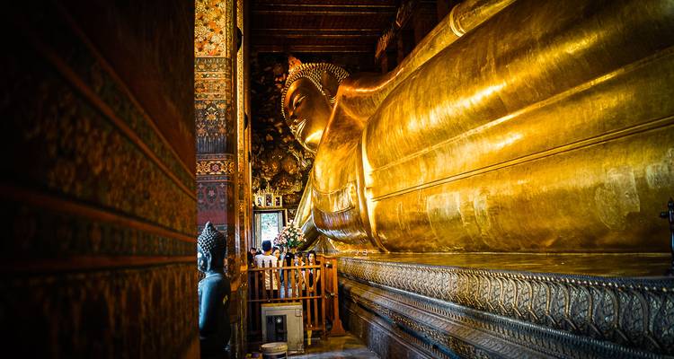 Side view of the golden Reclining Buddha statue surrounded by richly decorated temple walls.
