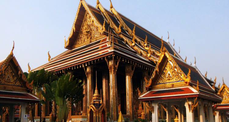 Ornate golden rooflines and columns of a grand Thai temple glowing in soft light.