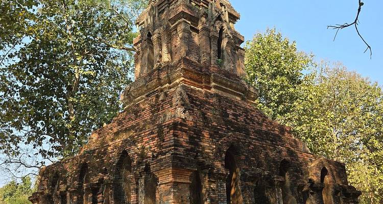 Weathered brick chedi partially hidden among tall green trees in an ancient Thai historical park.