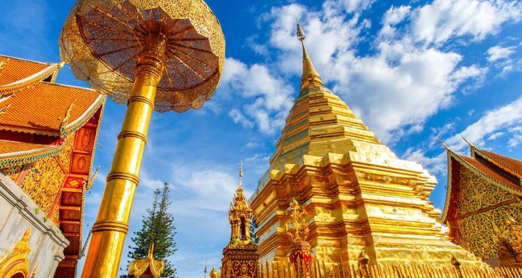 Golden stupa of Wat Phra That Doi Suthep soaring into a vivid blue sky with ornate umbrella in foreground.
