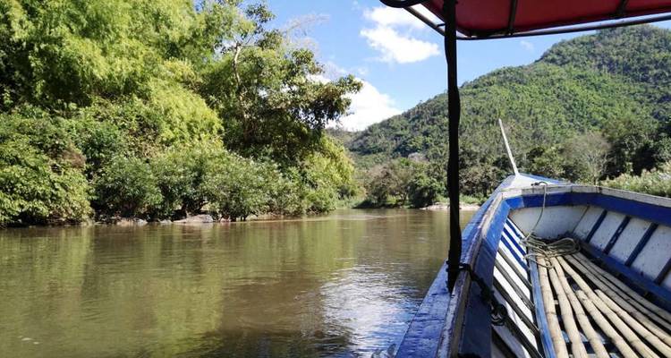Boat gliding along a calm jungle river with green hills under a bright sky.