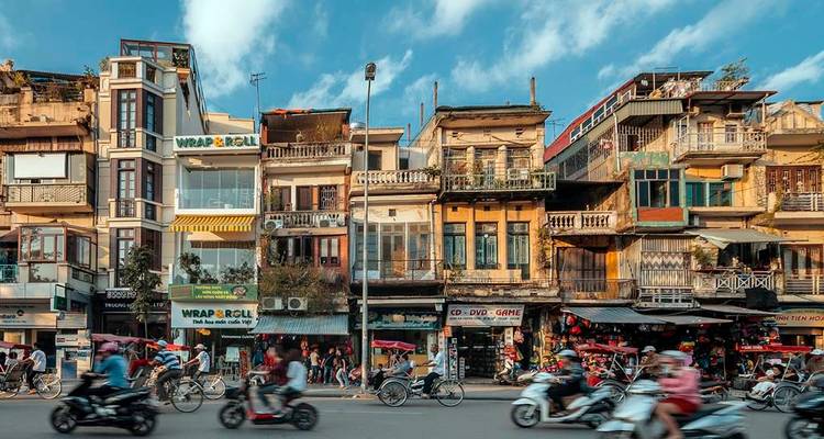 Drukke straat in Hanoi met smalle, kleurrijke winkelpandjes en vervagingde scooters die voorbij zoeven