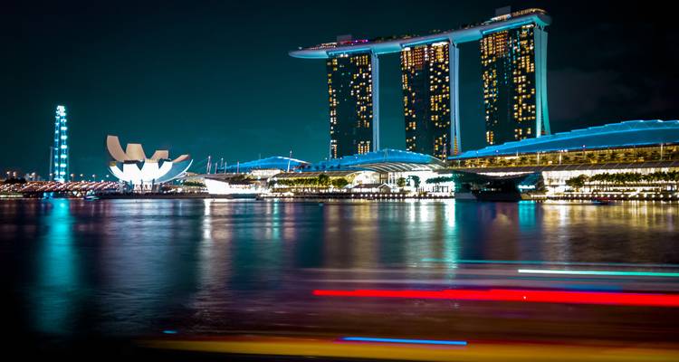Night view of Marina Bay Sands and ArtScience Museum reflecting on calm waters with colorful light streaks