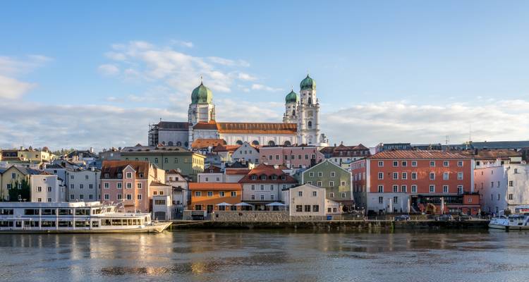 Charming European riverside town with colorful houses and twin-domed cathedral under a blue sky