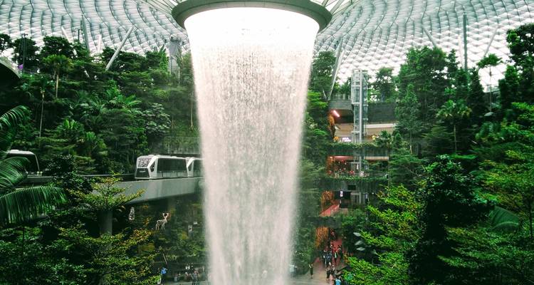 Spectacular indoor waterfall cascading from a circular oculus surrounded by lush greenery inside a glass-domed atrium