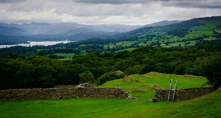 Lush green valleys, forests and a distant lake beneath moody clouds in England’s Lake District.