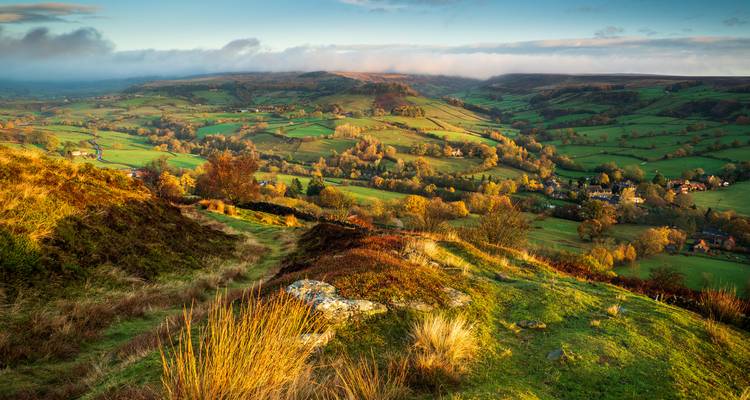 Golden-hour panorama of patchwork fields and valleys with autumn colours.