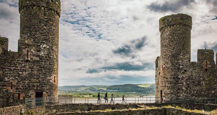 Visitors walk along the battlements between two massive stone towers at Conwy Castle.