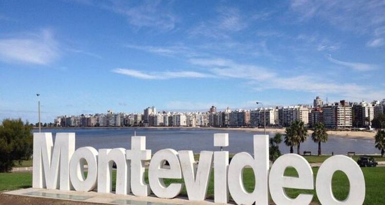 Large white Montevideo sign sits beside the waterfront with a skyline of apartments across the bay.