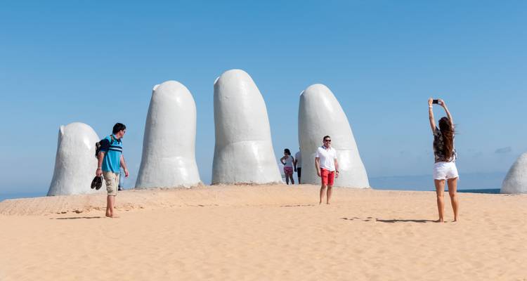 Tourists interact and pose around the famous giant hand sculpture emerging from the sand at Punta del Este’s beach.
