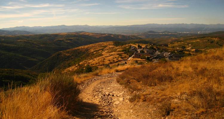 Mountainous golden landscape with winding path leading to a hilltop village