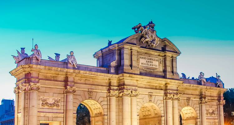 Illuminated Puerta de Alcalá monument against turquoise evening sky in Madrid