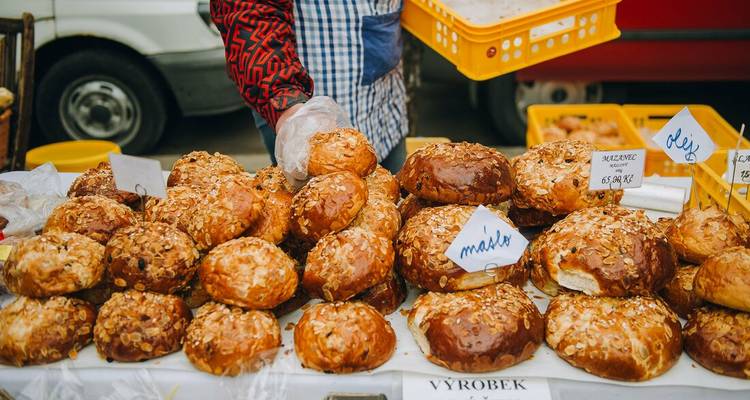 Étal de marché rempli de petits pains sucrés fraîchement cuits étiquetés en tchèque, avec un vendeur servant les clients.