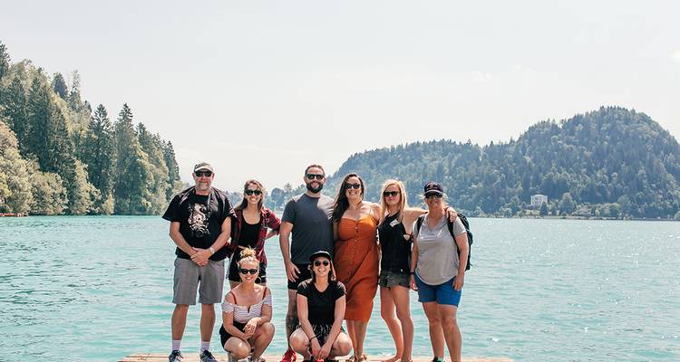 Eine kleine Reisegruppe posiert auf einem hölzernen Steg über dem türkisfarbenen Wasser des Bleder Sees.