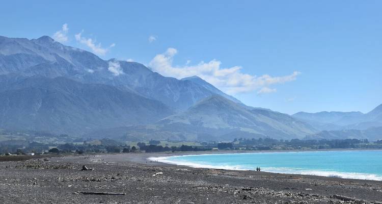 Raue Küstenlinie mit Steinstand, türkisfarbenem Wasser und bergigem Hintergrund in der Nähe von Kaikoura.