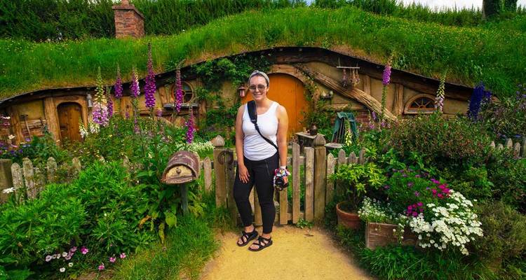 Ein Besucher posiert vor einem Hobbit-Loch mit bunten Blumen im Hobbiton Movie Set.