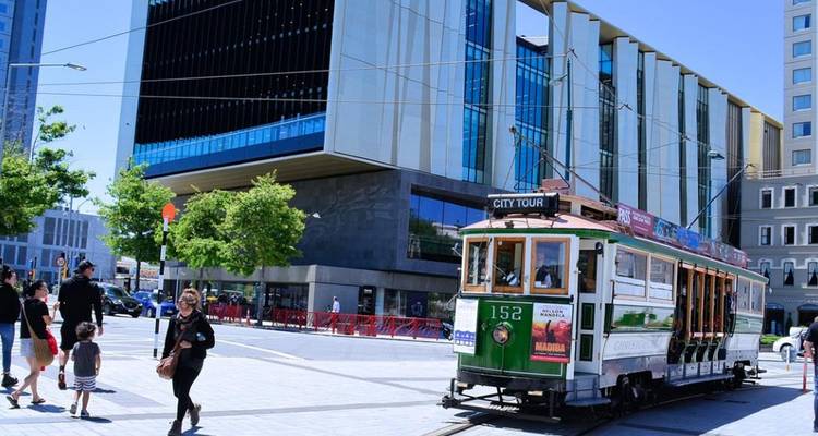 Historische grün-weiße Straßenbahn, die moderne Gebäude im Stadtzentrum von Christchurch passiert.