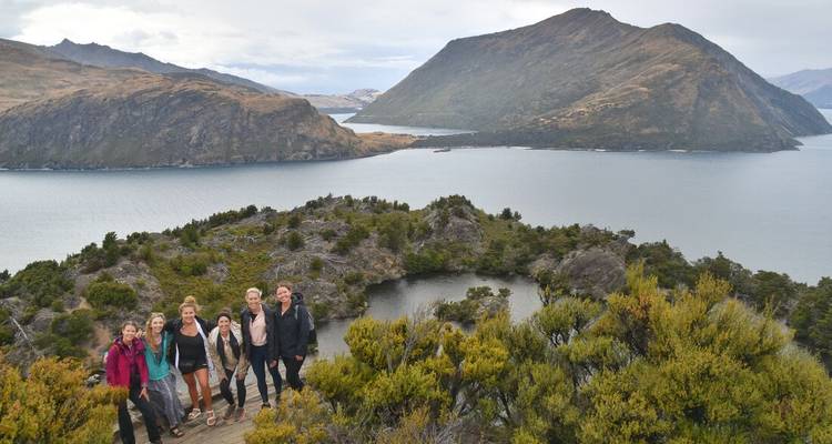 Small group of hikers standing on a high viewpoint overlooking a lake-dotted mountainous landscape.