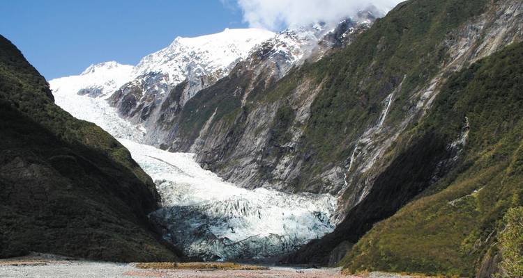 Massive white glacier spilling between steep green mountains beneath a partly cloudy sky.