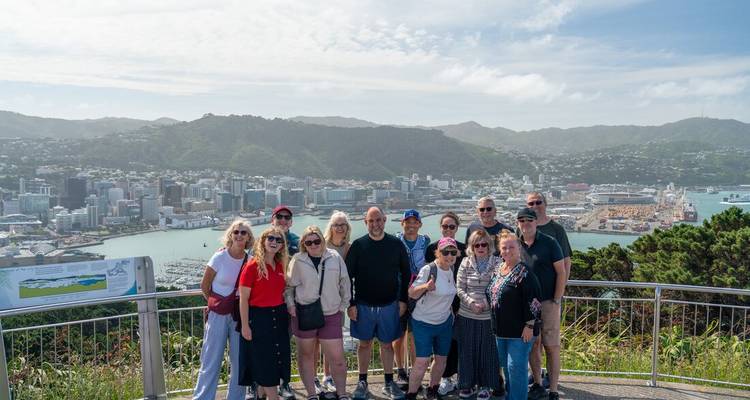 Un groupe de touristes pose à un belvédère avec les gratte-ciel de la ville, le port et les collines environnantes qui s'étendent en contrebas.