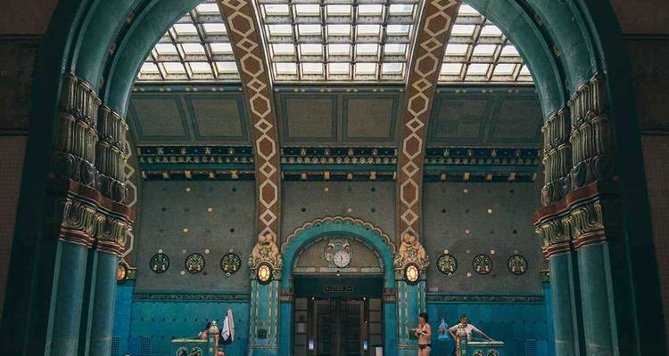 L'intérieur grand turquoise d'un bain thermal historique présente des carreaux de mosaïque et des bassins voûtés sous un plafond en verre.