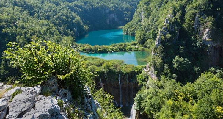 Turquoise tiered lakes and waterfalls framed by dense forest viewed from a high lookout in Plitvice.