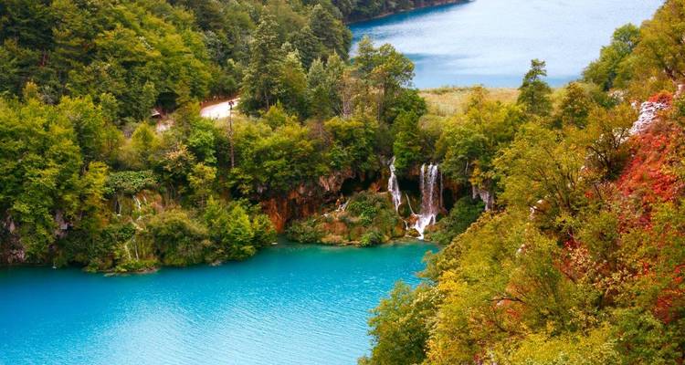 Vibrant teal lake with multiple small waterfalls framed by colourful autumn foliage in Plitvice.