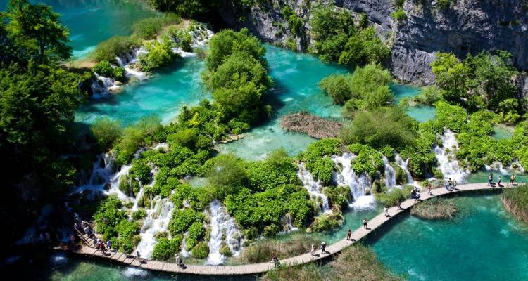 Bird’s-eye view of visitors crossing a wooden walkway over cascades and turquoise pools in Plitvice Lakes.
