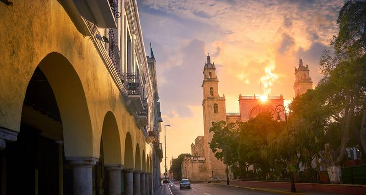 Goudkleurig zonsonderganglicht baadt Mérida's kathedraaltorentjes en koloniale galerijen langs een rustige straat.