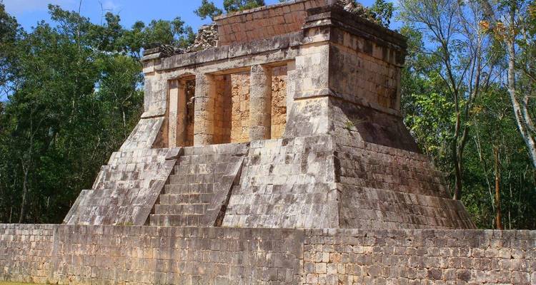 Een klein trapvormig Maya-tempel staat te midden van dicht junglegroen op het Yucatán-schiereiland.