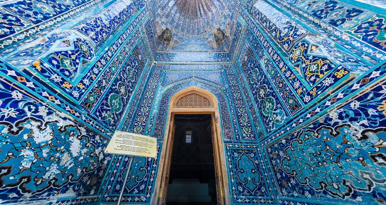 Ein schmaler Innenflur, der vollständig mit lebendigen blauen Mosaiken und geometrischen Mustern bedeckt ist und zu einer Holztür führt.