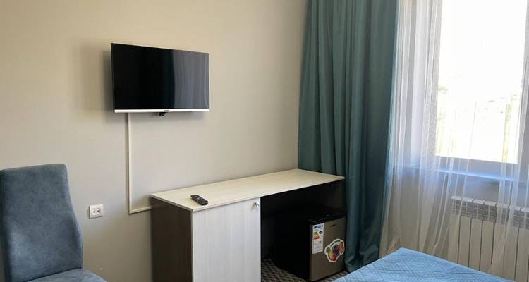 Nahaufnahme einer Hotelzimmerecke mit einem über einem minimalistischen Schreibtisch montierten Fernseher neben einem sonnigen Fenster.