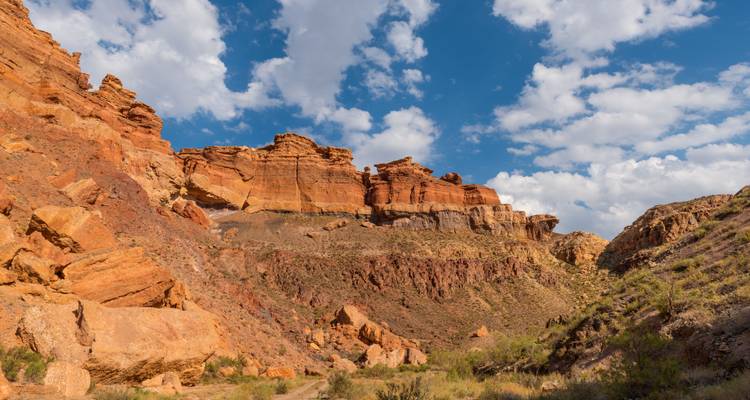 Unter einem strahlend blauen Himmel erheben sich raue, rötliche Sandsteinformationen im Charyn Canyon.