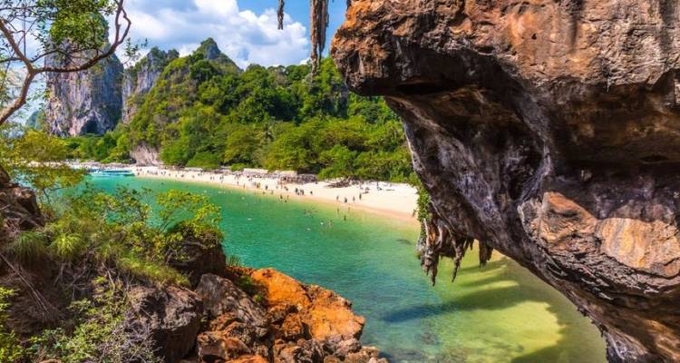 Vue depuis l'ouverture d'une grotte calcaire vers une plage de sable blanc et une eau d'émeraude parsemée de touristes