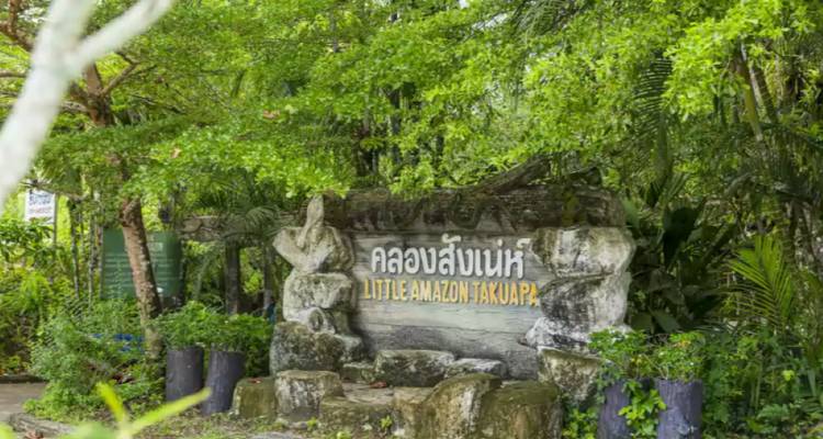 Panneau d'entrée en pierre portant l'inscription « Petite Amazonie Takuapa » entouré d'une végétation tropicale luxuriante
