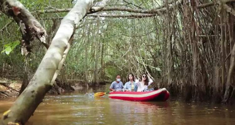 Un petit groupe pagayant dans un kayak gonflable rouge le long d'une voie navigable étroite dans la jungle sous des branches basses