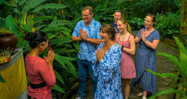 Group of travelers greet a Balinese host with palms together amid lush tropical gardens.