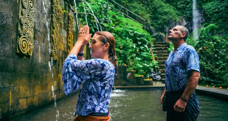 Couple performs purification ritual at a sacred water temple surrounded by lush greenery