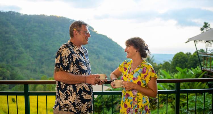 Smiling couple enjoying coffee on balcony overlooking green valley and hills