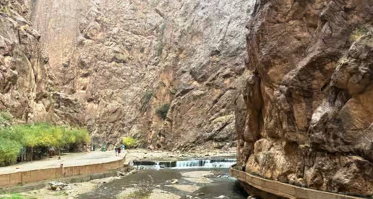 Narrow river and pathway running through towering vertical canyon walls at Todra Gorge.