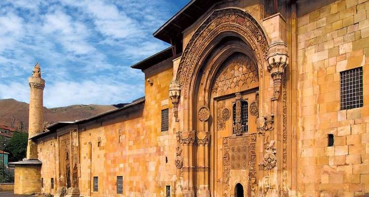Intricately carved stone portal of a historic Anatolian medrese against blue sky.