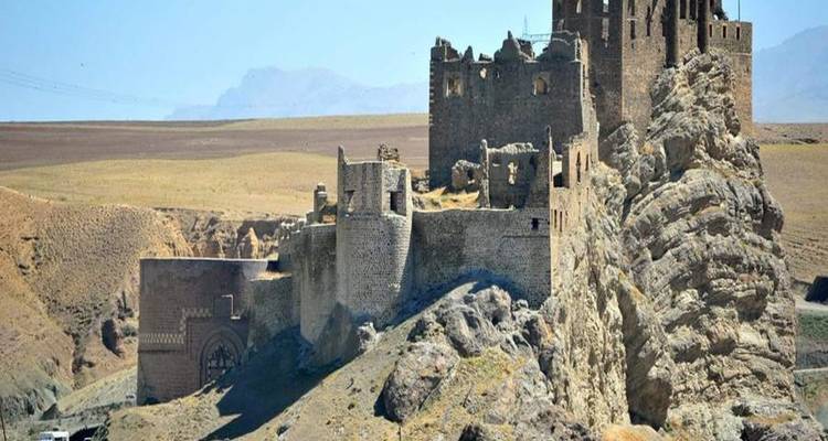 Stone castle ruins perched on rocky outcrop overlooking dry plains.