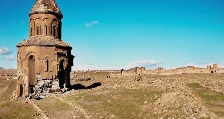 Solitary ancient church ruin standing on windswept plain with blue sky backdrop.