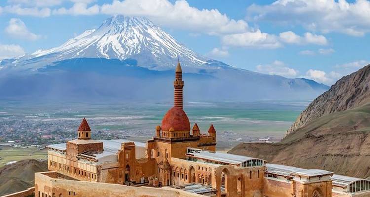 Ishak Pasha Palace with distinctive red dome set before snow-capped Mount Ararat and expansive valley.