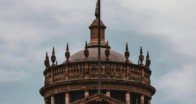 Cúpula de piedra y aguja de un edificio histórico recortadas contra un cielo nublado