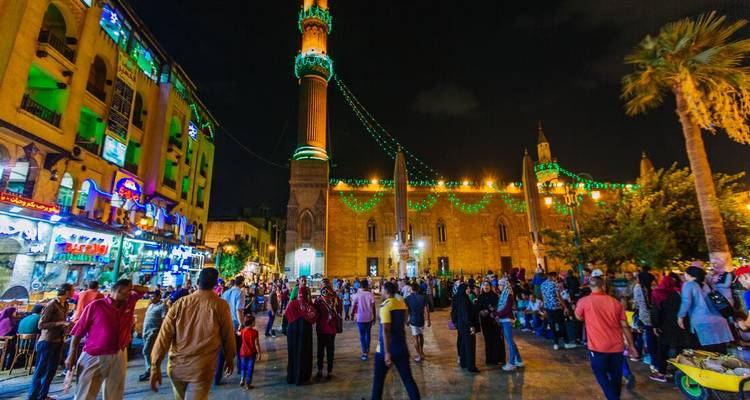 Lebendige Nachtszene vor einer Moschee in Kairo mit Menschenmengen und grünen Festlichkeitslichtern.