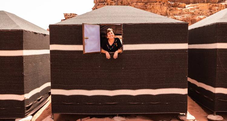 Eine lächelnde Frau lehnt sich aus dem Fenster eines schwarz-weißen Beduinenzelte in Wadi Rum.