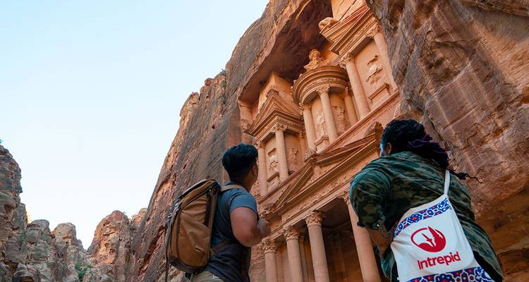 Zwei Rucksacktouristen blicken auf dem engen Canyonboden bewundernd auf die majestätischen Steinsäulen des Schatzes von Petra hinauf.