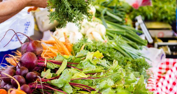 Fresh colourful vegetables including beets, carrots and leafy greens are displayed on a market stall table.